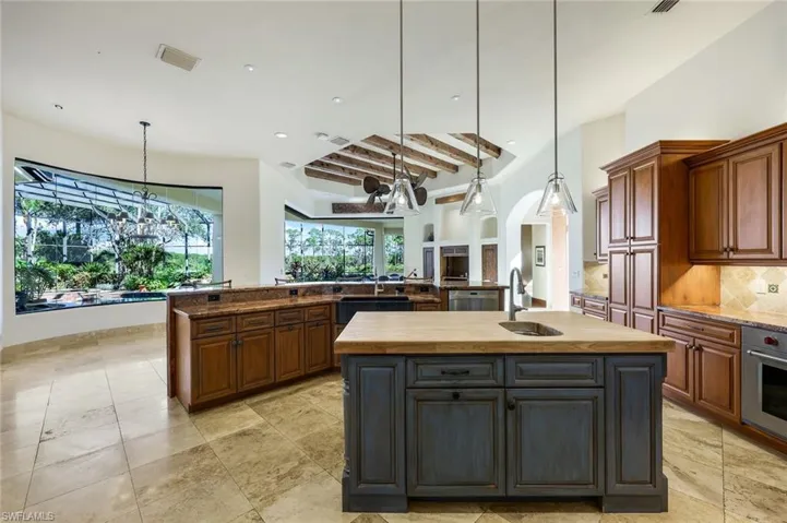 Kitchen with a center island with sink, oven, pendant lighting, and beamed ceiling