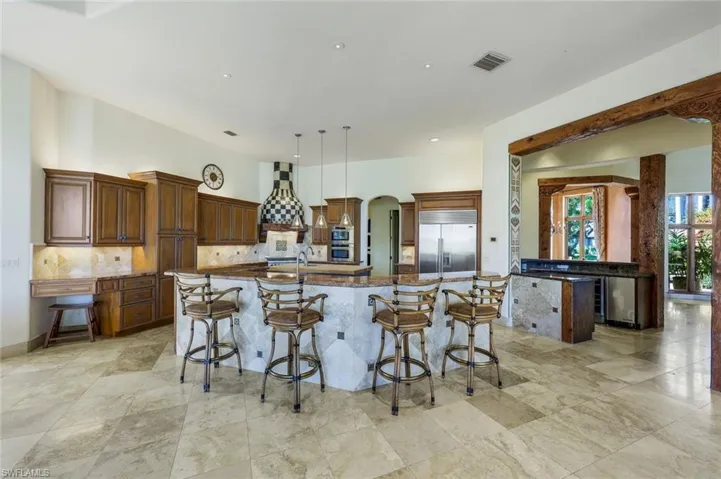 Kitchen with a kitchen breakfast bar, stainless steel built in fridge, a large island, and light stone counters