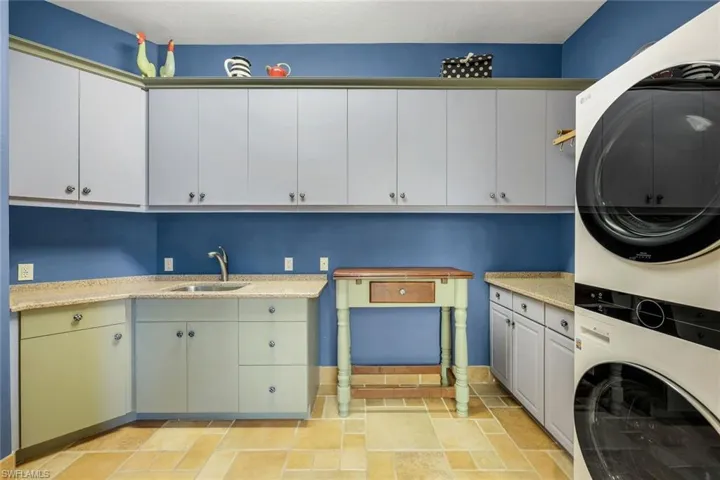 Laundry room with cabinets, stacked washing maching and dryer, and sink