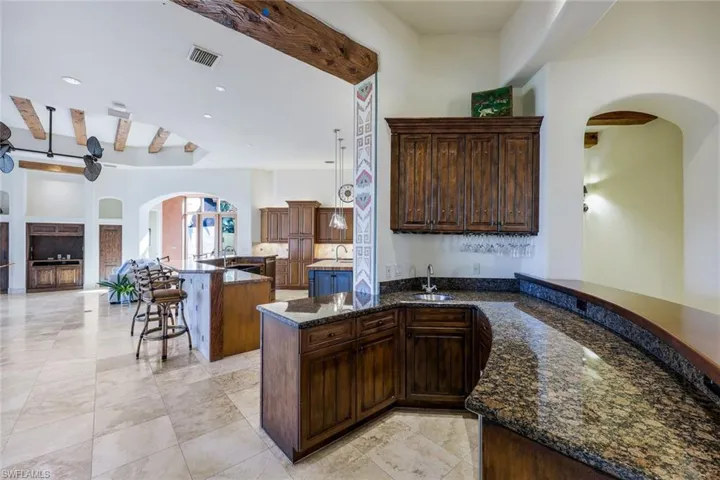 Kitchen featuring kitchen peninsula, dark stone counters, dark brown cabinets, sink, and beam ceiling