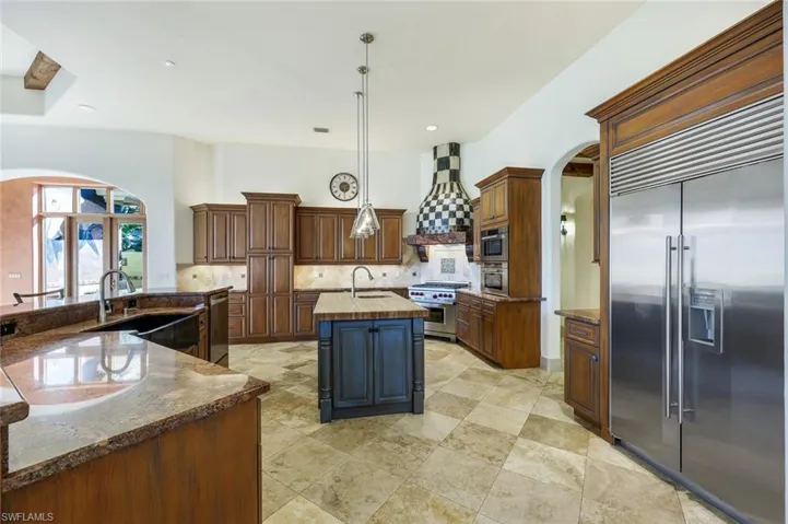 Kitchen with custom exhaust hood, high end appliances, sink, decorative light fixtures, and an island with sink