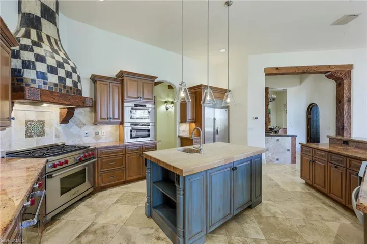 Kitchen with wooden counters, custom range hood, premium appliances, a kitchen island with sink, and sink