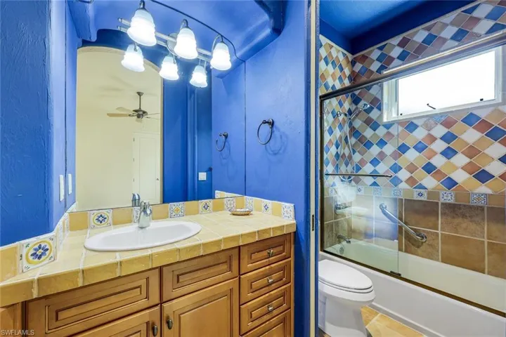 Full bathroom with tile patterned floors, vanity, ceiling fan, shower / bath combination with glass door, and toilet