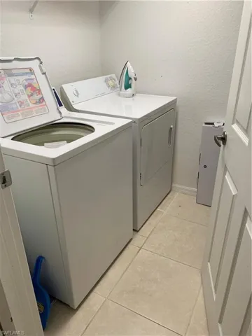 Laundry area with a textured wall, light tile patterned floors, and washer and clothes dryer