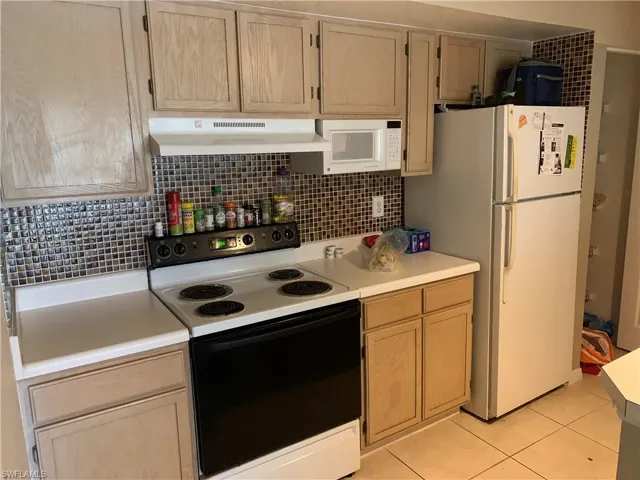 Kitchen with light wood finish cabinets, white appliances, light countertops, and backsplash