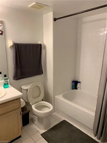 Bathroom featuring vanity, shower / tub combo with curtain, light tile patterned flooring, a textured ceiling, and a textured wall