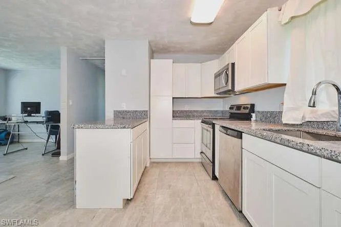 Kitchen with stainless steel appliances, white cabinets, an office area, and light stone countertops