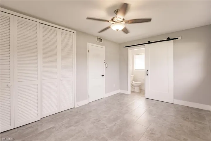 Unfurnished bedroom featuring a barn door, a closet, a ceiling fan, and ensuite bathroom