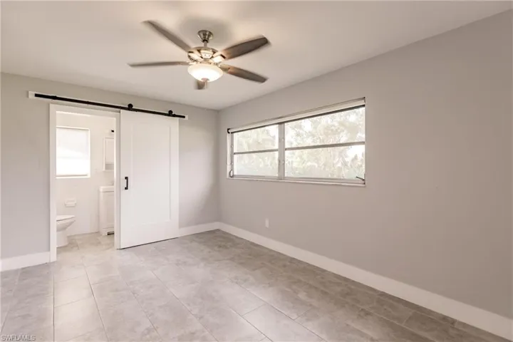 Unfurnished bedroom with ceiling fan, a barn door, connected bathroom, and light tile patterned floors
