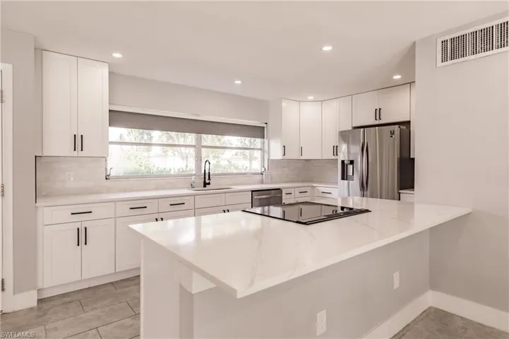 Kitchen featuring white cabinets, appliances with stainless steel finishes, light stone countertops, recessed lighting, and tasteful backsplash