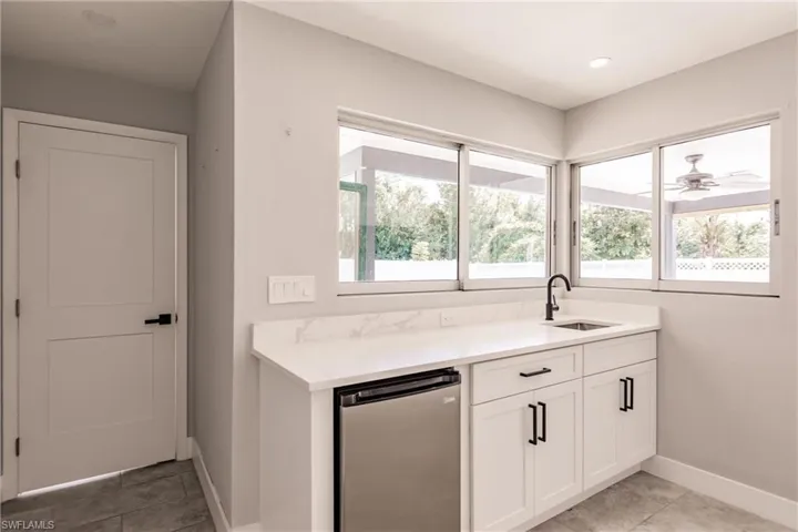 Kitchen featuring light tile patterned floors, dishwasher, white cabinetry, light stone countertops, and ceiling fan