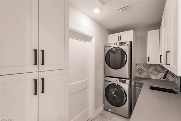 Washroom featuring stacked washer / drying machine, cabinet space, and light tile patterned floors
