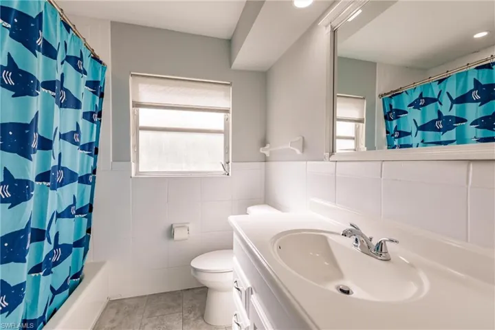 Full bath with tile walls, a wainscoted wall, vanity, shower / tub combo, and light tile patterned floors