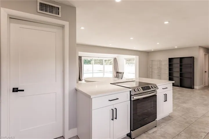Kitchen featuring stainless steel electric stove, white cabinetry, a peninsula, recessed lighting, and light stone counters