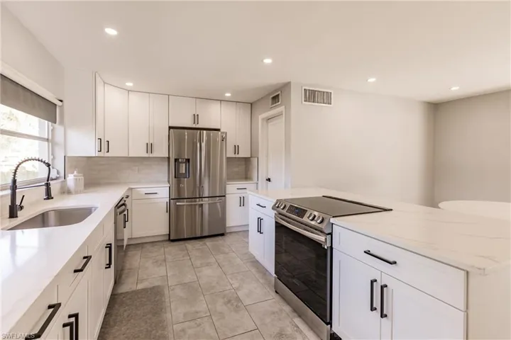Kitchen featuring appliances with stainless steel finishes, light stone countertops, white cabinets, a kitchen island, and recessed lighting