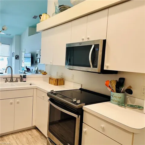Kitchen with stainless steel appliances, light countertops, white cabinetry, and light wood-style floors
