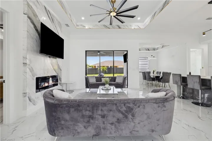 Tiled living room with crown molding, ceiling fan, a raised ceiling, and a high end fireplace