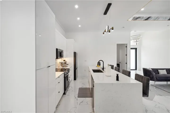Kitchen featuring light tile patterned flooring, white cabinets, an island with sink, appliances with stainless steel finishes, and decorative light fixtures