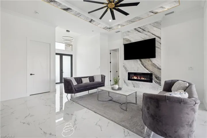 Living room featuring a premium fireplace, tile patterned flooring, ceiling fan, a raised ceiling, and ornamental molding