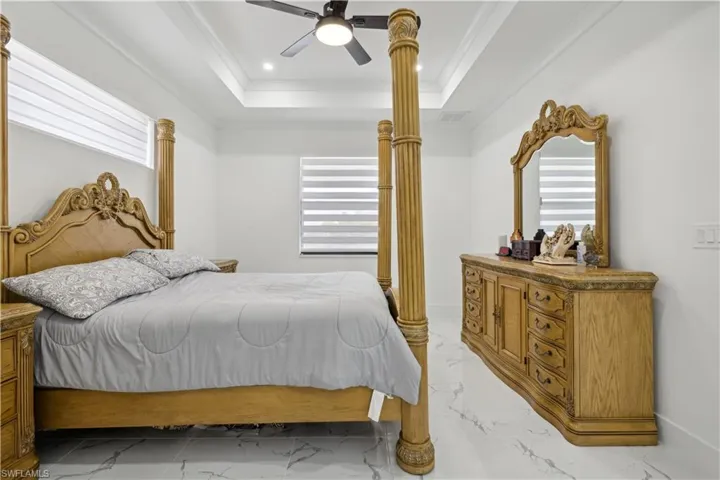 Tiled bedroom featuring ceiling fan, multiple windows, a tray ceiling, and ornamental molding
