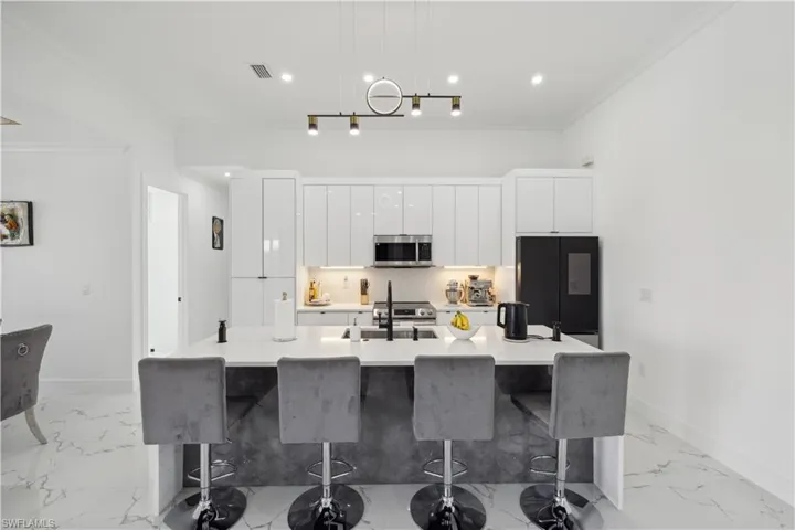 Kitchen featuring decorative light fixtures, stainless steel appliances, a breakfast bar, a large island with sink, and light tile patterned floors