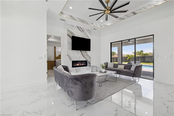 Living room with light tile patterned floors, ceiling fan, a tray ceiling, a premium fireplace, and ornamental molding
