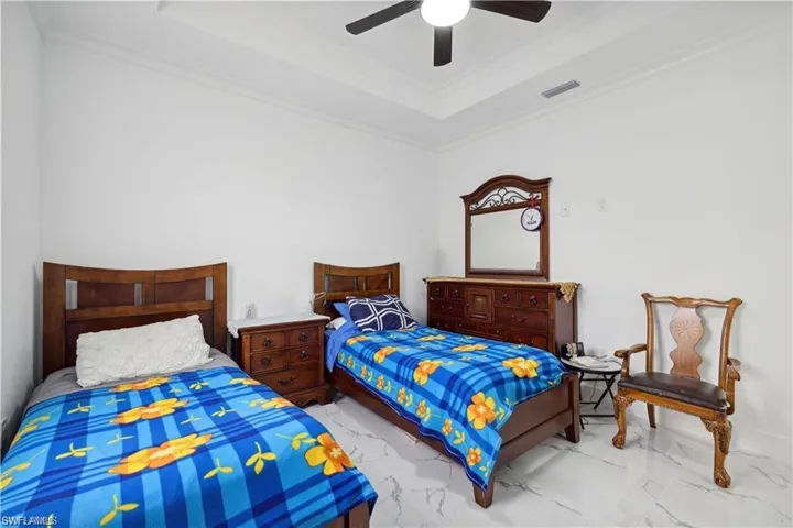 Bedroom with crown molding, a tray ceiling, tile patterned flooring, and ceiling fan