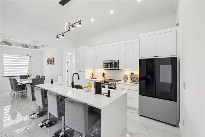 Kitchen featuring white cabinetry, stainless steel appliances, pendant lighting, an island with sink, and a kitchen breakfast bar
