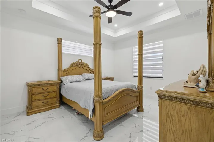 Bedroom with ceiling fan, a raised ceiling, and light tile patterned floors