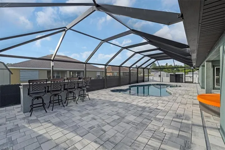 Screened outdoor living area featuring a custom-shaped swimming pool, paver patio, integrated bar seating, and a covered lanai extension