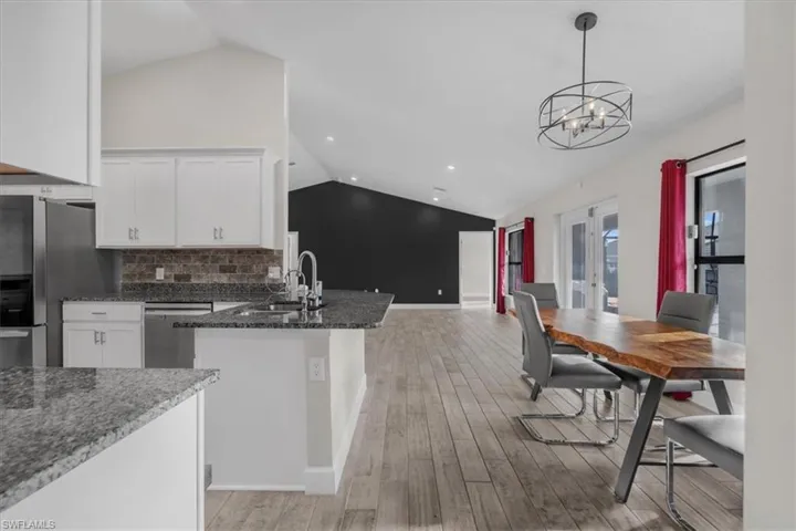 Open-concept living area featuring vaulted ceilings, wood-finish flooring, a kitchen island with granite countertops, stainless steel appliances, and French doors