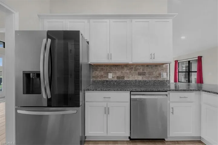 Contemporary kitchen featuring white shaker cabinetry, stainless steel appliances, speckled stone countertops, and a brick-patterned backsplash