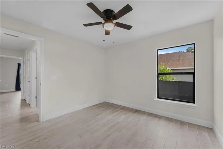 Spacious room featuring wood-finish tile flooring, a dark-framed window, a ceiling fan with integrated lighting, and neutral wall tones