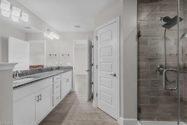 Bathroom featuring a double vanity with granite-style countertop, dual undermount sinks, and white cabinetry