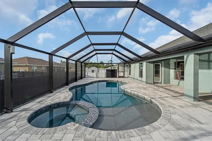 Screened lanai featuring a freeform swimming pool with integrated spa, paver decking, and direct access to the home
