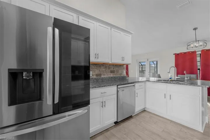 Modern kitchen featuring white cabinetry, granite-style countertops, and a full stainless steel appliance suite including a refrigerator and dishwasher