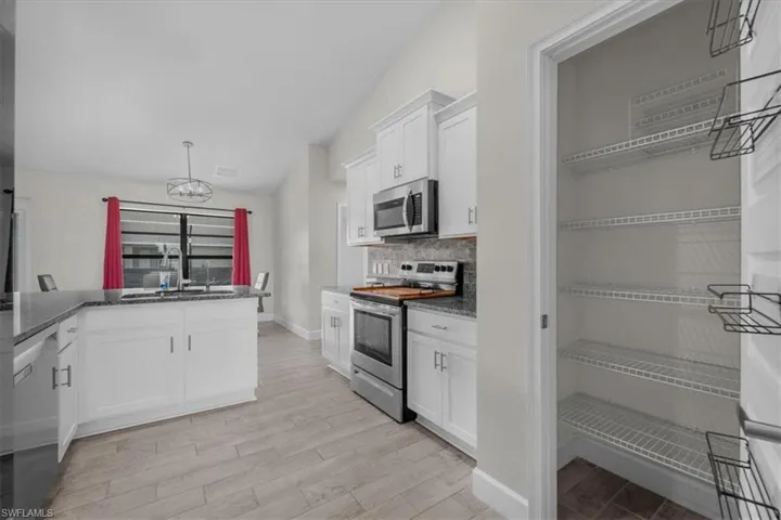 Kitchen featuring white cabinetry, dark speckled countertops, stainless steel appliances, and wood-finish flooring