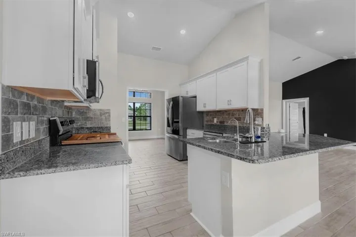 Kitchen featuring granite countertops, stainless steel appliances, white cabinetry, and wood-finish tile flooring