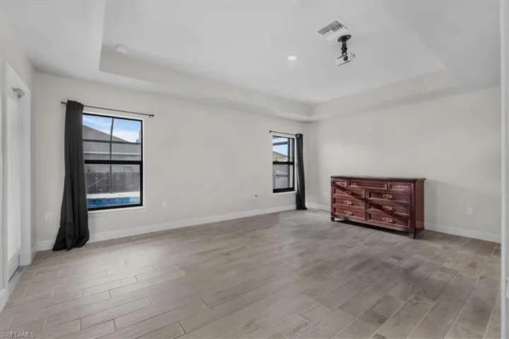 Spacious room featuring wood-finish tile flooring, a tray ceiling with recessed lighting, and a built-in projector