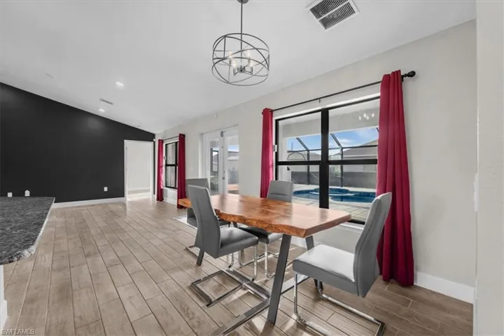 Open-concept interior featuring wood-finish flooring, a vaulted ceiling, a contemporary light fixture, and large windows overlooking a screened pool area