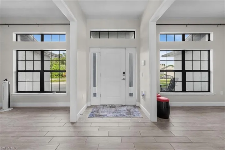 Entryway featuring a white paneled door with frosted sidelights, transom windows, and dark-framed grid windows