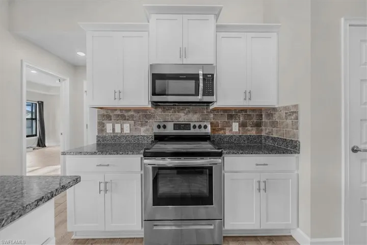Kitchen featuring white shaker-style cabinetry, stainless steel appliances, granite countertops, and a subway tile backsplash