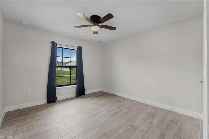 Neutral-toned interior featuring wood-finish flooring, a ceiling fan with integrated lighting, and a window with a grid pattern