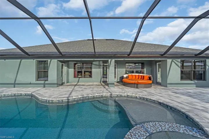 Expansive screened lanai featuring a swimming pool, integrated spa with mosaic tile detailing, and a paver deck