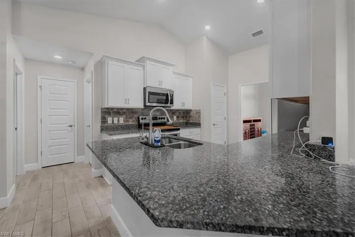 Spacious kitchen featuring a large island with a dark speckled countertop, wood-finish flooring, white cabinetry, a stainless steel microwave, and a tiled backsplash