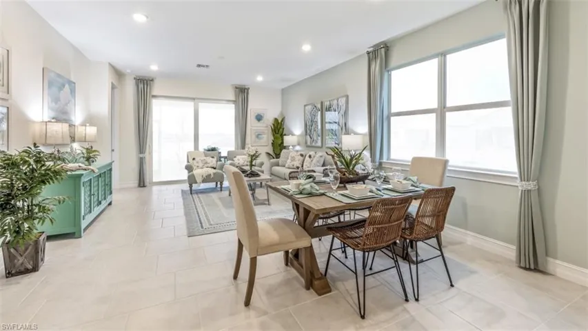 Expansive open-concept living area featuring large format tile flooring, a dining space with a rustic wood-finish table, and a living room with sliding glass doors