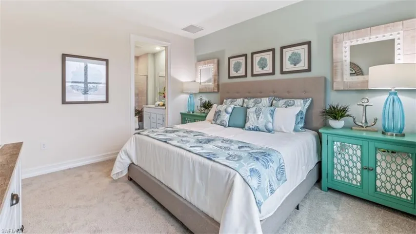 Wall-to-wall carpeting, upholstered headboard, recessed ceiling lighting, and a doorway to a bathroom with a vanity