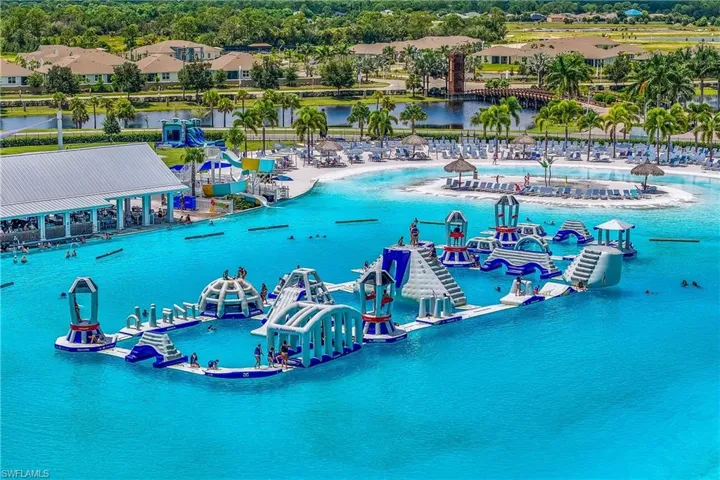 Expansive lagoon with an inflatable obstacle course, adjacent beach area, and multiple shaded lounge areas