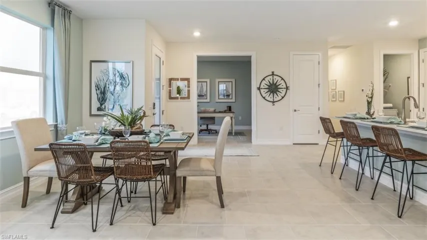 Open-concept layout featuring light-toned tile flooring, recessed lighting, a dining area, and a kitchen island with seating