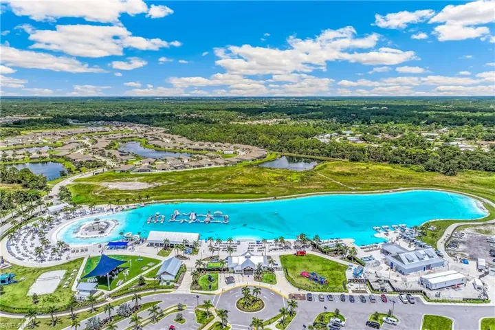 Aerial perspective showcasing a large turquoise lagoon with a white sand-finish beach area, surrounded by lush green landscaping and mature palm trees